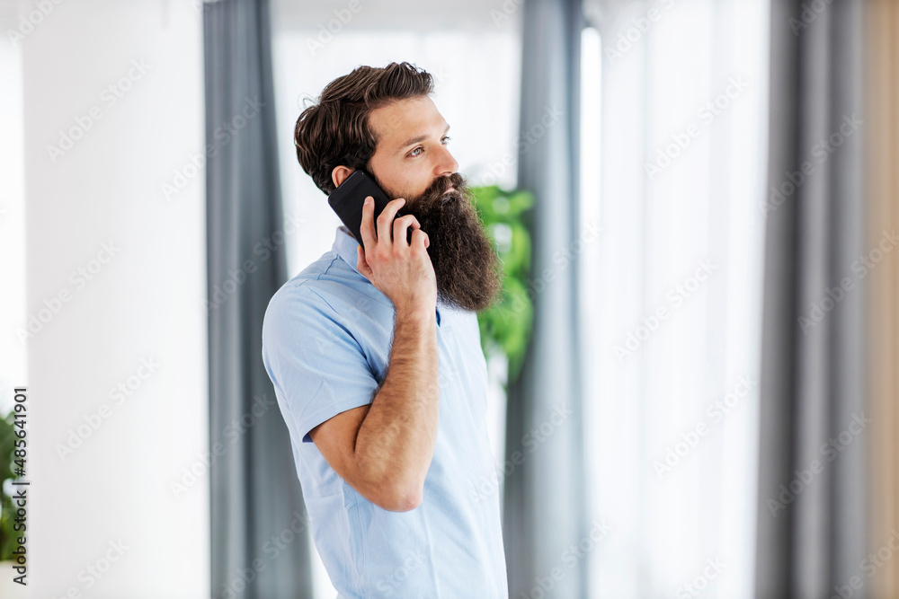 Serious bearded man standing at his home and having phone call. Serious bearded man standing at his home and having phone call.