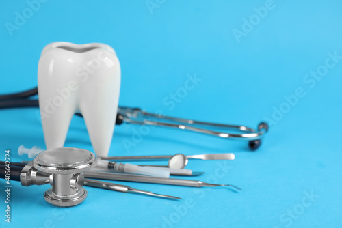 Tooth shaped holder, different dentist's tools and stethoscope on light blue background. Space for text © New Africa