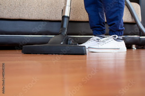 Woman using vacuum cleaner to cleaning parquet floor.