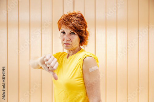 A serious woman showing her shoulder after the vaccine and gesturing thumbs down. 