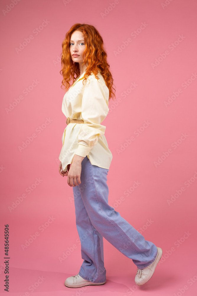 Full-length side view photo of a serious reahead lovely girl in modern clothes looking at the camera over pink background, beautiful hairstyle concept. Full-length side view photo of a serious reahead lovely girl in modern clothes looking at the camera over pink background, beautiful hairstyle concept.