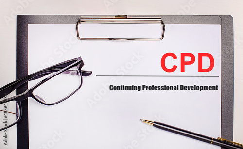 On a light wooden background glasses, a pen and a sheet of paper with the text CPD Continuing Professional Development. Business concept photo