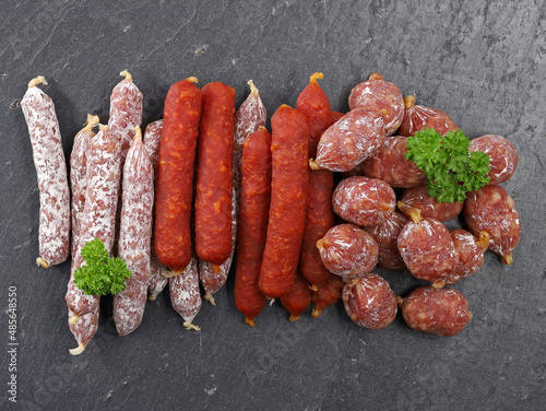 various meat snacks composition, top view of serveral air dried mini salamis on black slate plate