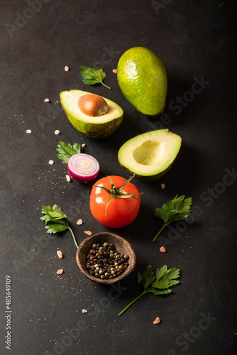 Fresh ingredients for guacamole: avocado, tomato,red onion, cilantro on a black background. With space for text.