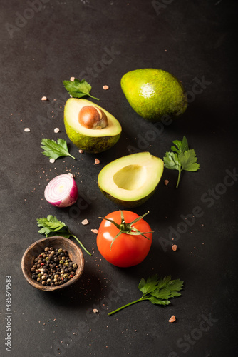 Fresh ingredients for guacamole: avocado, tomato,red onion, cilantro on a black background. With space for text.