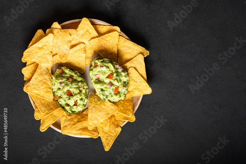 Traditional latinamerican sauce guacamole in cut half avocado, mexican nachos chips on dark background.