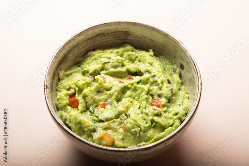 Traditional Mexican Guacamole sauce made from avocado. lime, red onion, tomatoes, cilantro on a pink background.