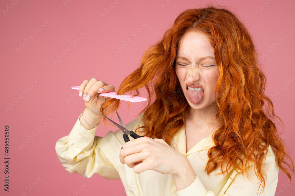Redhead girl with dislike facial expression holding the hairdresser instruments in her hands, cut hair in a beauty salon concept.