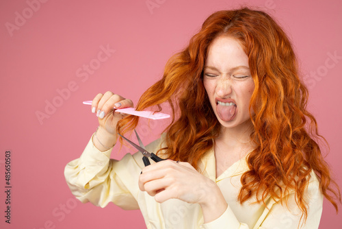 Obraz na płótnie Redhead girl with dislike facial expression holding the hairdresser instruments in her hands, cut hair in a beauty salon concept. w salonie