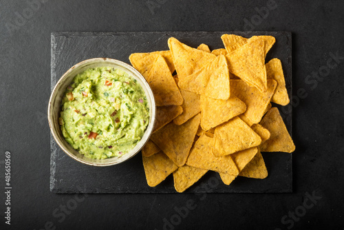 Mexican nachos chips and bowl with homemade fresh guacomole sauce made from avocado and lime  over black background.