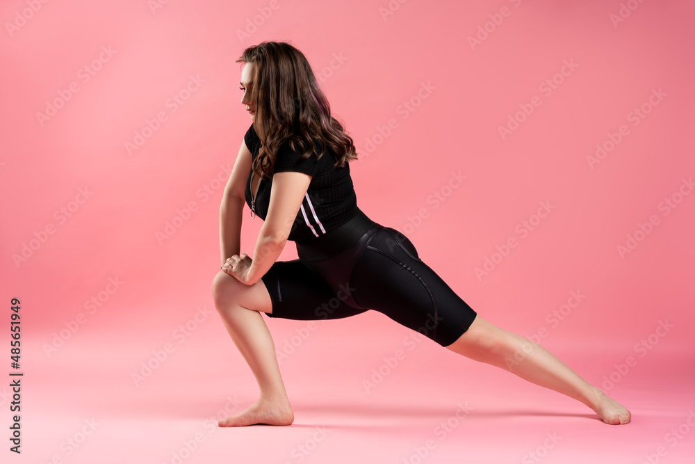 Fitness plus size model in black sportswear on pink background