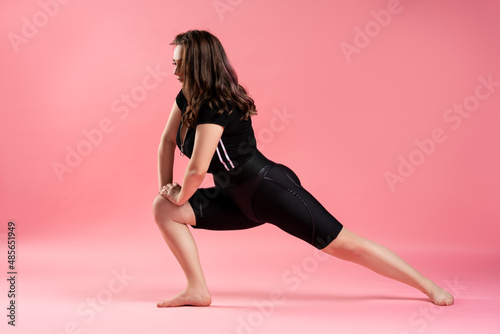 Fitness plus size model in black sportswear on pink background