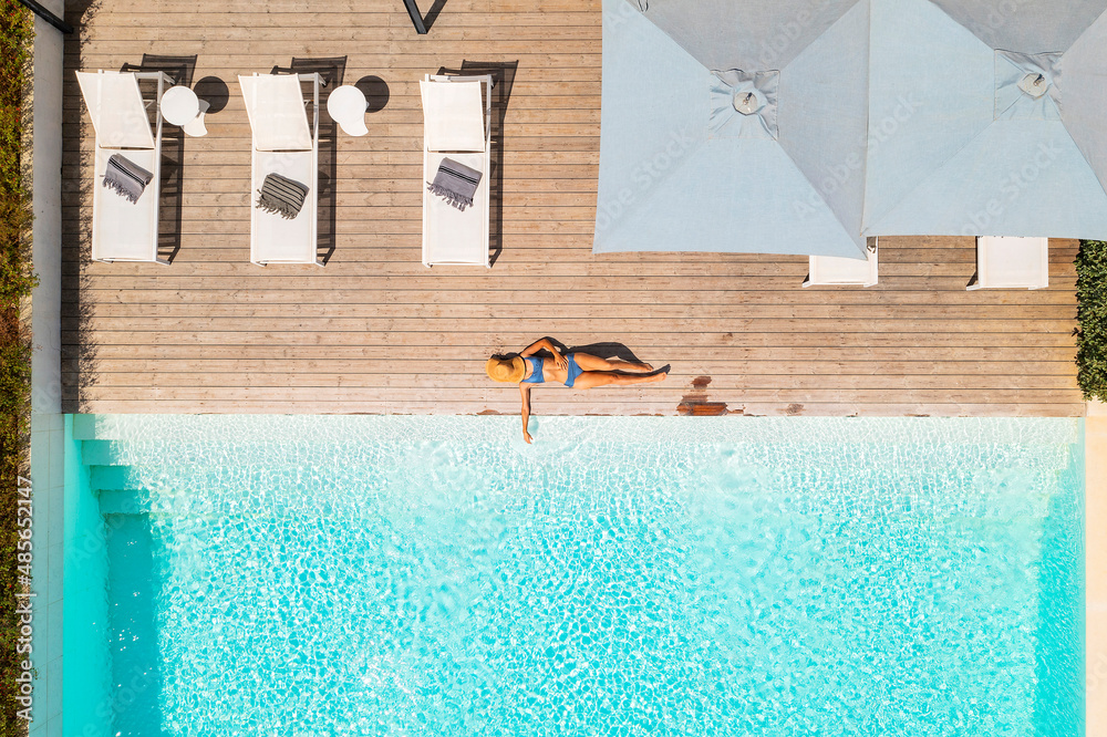 Aerial view of a blonde woman relaxing along the swimming pool of a ...
