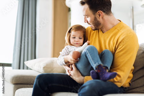 Young father having fun while playing with his little daughter on sofa at home
