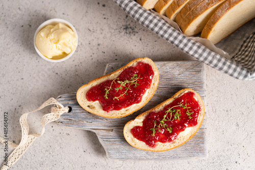 White bread slices with butter and raspberry jam on it, greens on wooden board, organic country sweet sandwich, homemade dessert. Copy space.