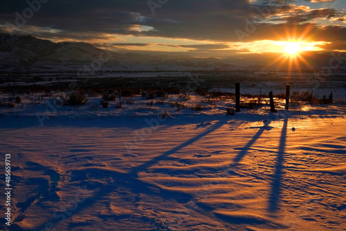 Sunrise or Sunset Sunlight Fenceposts Shadows Across the Snow Ground