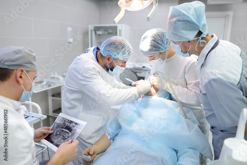 Surgeons and nurse during a dental operation. Medical team performing surgical dentistry operation. Anesthetized patient in the operating room. Installation of dental implants in the clinic.
