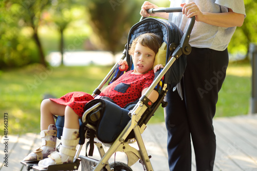 A woman with a disabled girl in a wheelchair walking in the park summer. On baby legs orthosis. Child cerebral palsy. Treatment and rehabilitation of CP. Handicapped kid. photo