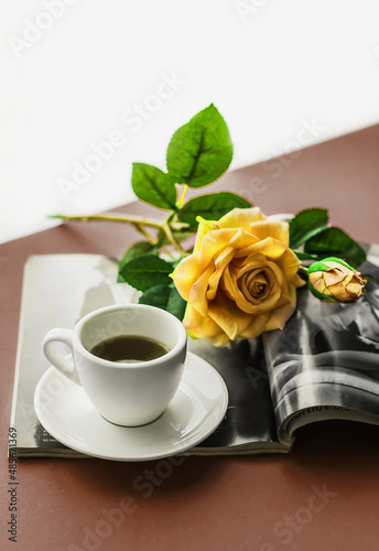 Romantic atmosphere. A cup of coffee with a saucer and a rose flower in a fashion magazine on a colored background. Happy birthday banner concept, mother's day, valentine's day. Lifestyle. 