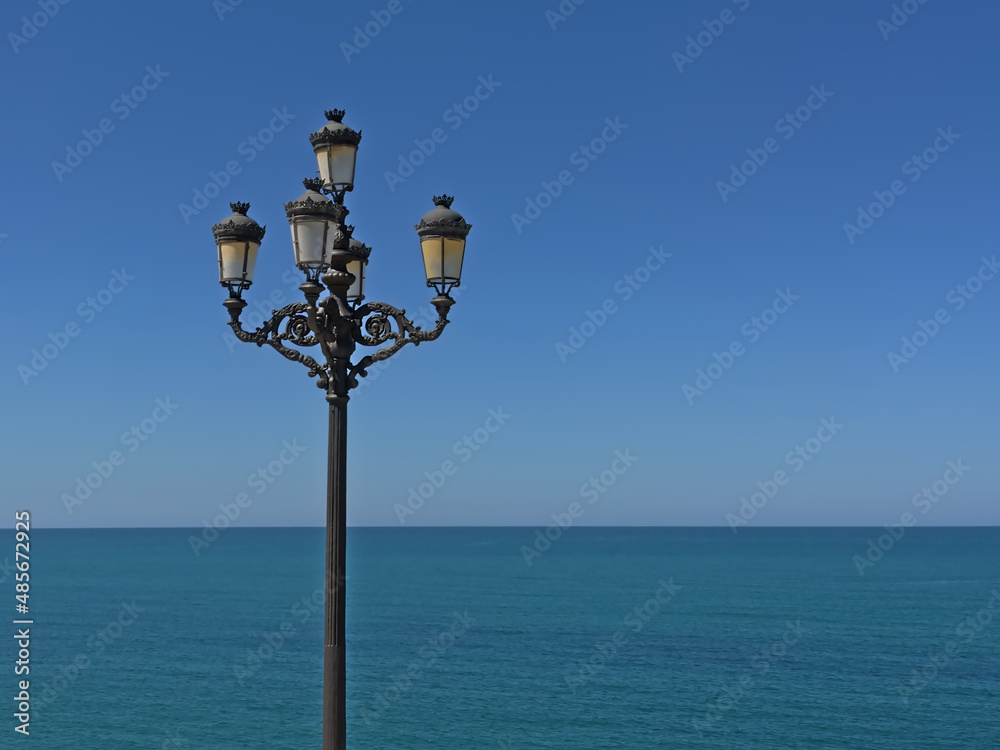 Retro street lanterns in front of a deep blue sea and sky on the coast of Cadiz, Andalusia, Spain 