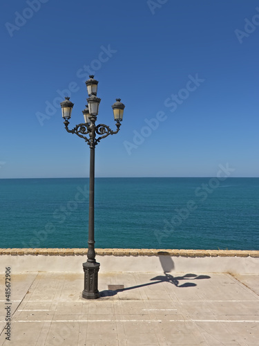 Retro street lanterns in front of a deep blue sea and sky on the coast of Cadiz, Andalusia, Spain 