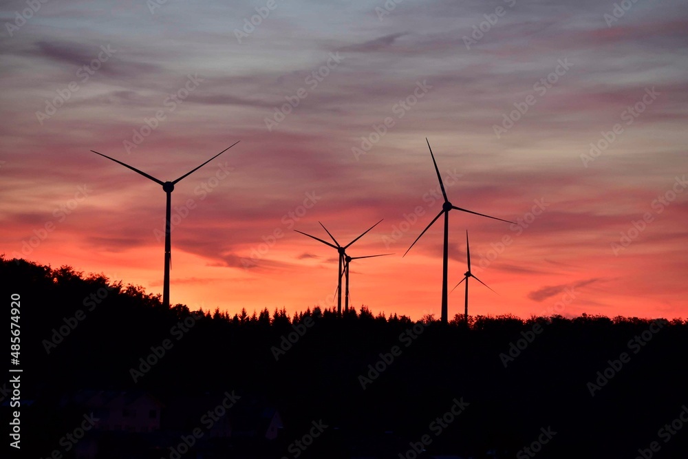 Windkrafträder in einem Windpark mit Abendrot und dunklen Wolken Windkrafträder in einem Windpark mit Abendrot und dunklen Wolken