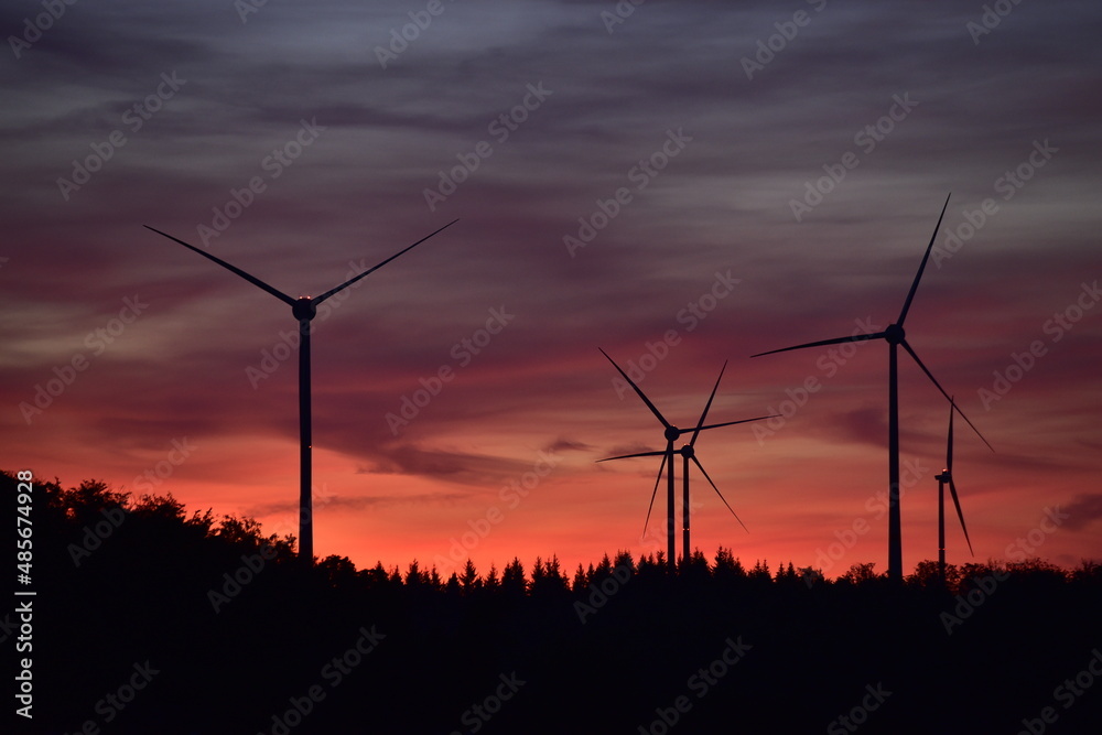 Windkrafträder in einem Windpark mit Abendrot und dunklen Wolken Windkrafträder in einem Windpark mit Abendrot und dunklen Wolken
