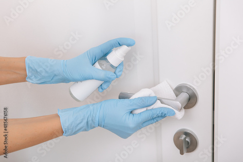 Cleaning black door handle with an antiseptic wet wipe, blue gloves and sanitizer. Woman hand using towel for cleaning. Sanitize surfaces prevention in hospital and public spaces against corona virus
