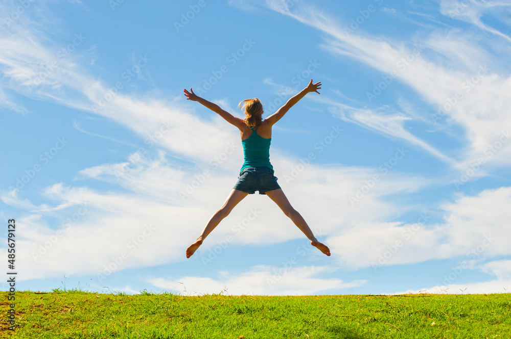 Happy woman jumping for joy, celebrating winning and enjoying happiness of freedom and carefree lifestyle on green grass with blue sky, background with copy space Happy woman jumping for joy, celebrating winning and enjoying happiness of freedom and carefree lifestyle on green grass with blue sky, background with copy space