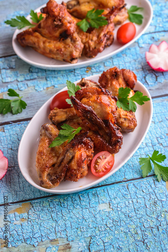 Baked crispy chicken wings in a white plate on a blue background with copy space