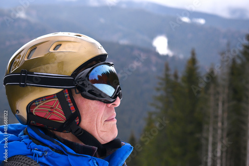 Active old aged senior experienced mature snowboarder skier man in protection helmet,goggles enjoying mountain peak,slope, winter extreme sport activities at alpine skiing resort. stunning panoramic