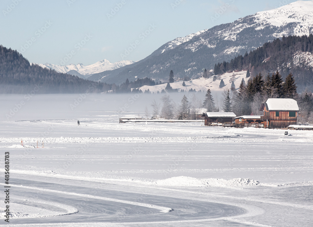 early morning at the frozen alpine lake in Austria in winter with snow and fog