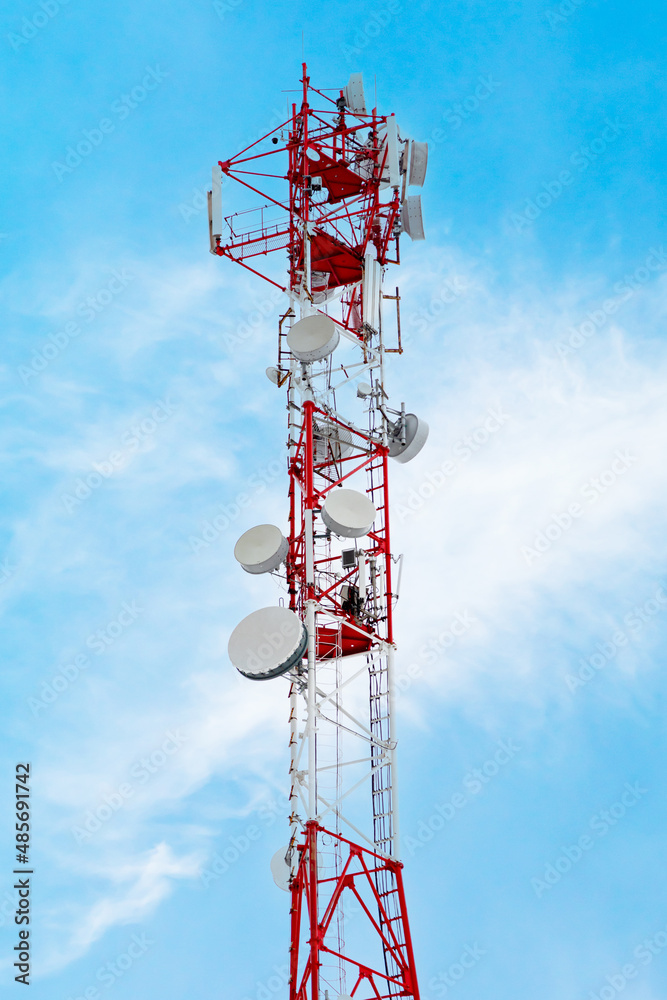 Telecommunication tower with radio relay communication antennas and 4G, 5G transmitters. Cellular base station with transmitter antennas on a high red and white metal telecommunication tower. Telecommunication tower with radio relay communication antennas and 4G, 5G transmitters. Cellular base station with transmitter antennas on a high red and white metal telecommunication tower.