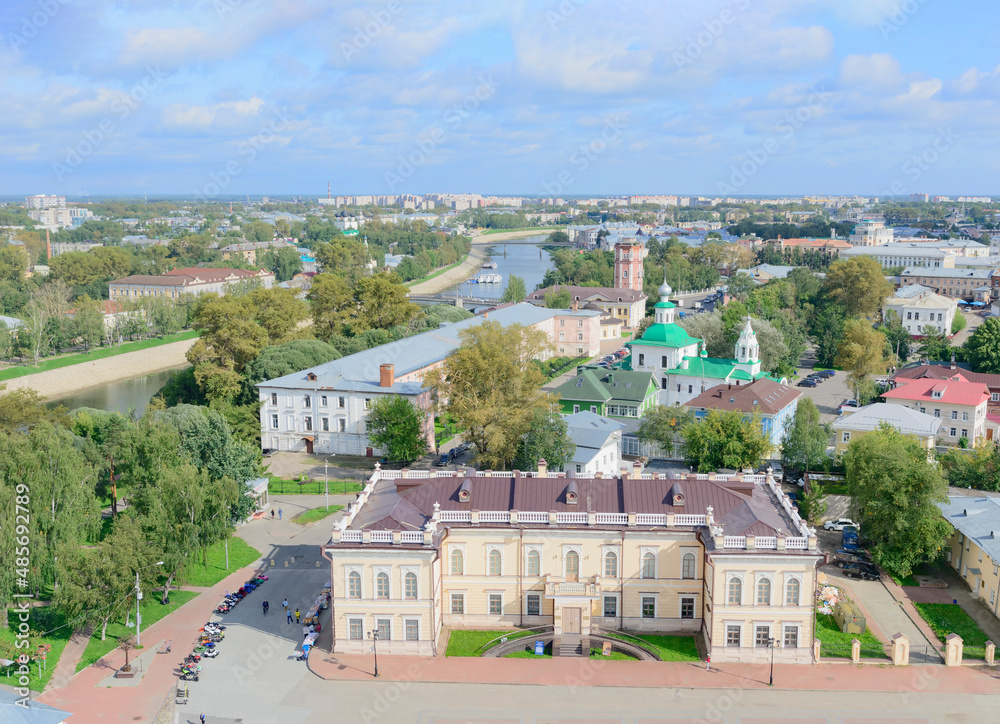 Aerial view of the old town of Vologda, Russia. Blue sky with clouds, green trees and grass, white church walls and towers, green and red roofs, blue water of Vologda river