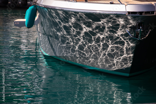 The mesmerizing reflection of the water on the glossy side of a huge yacht anchored, chrome details photo