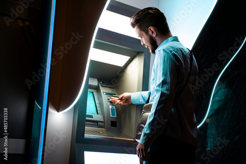 Cuadro en lienzo Back view modern neat young man putting credit card into the ATM machine