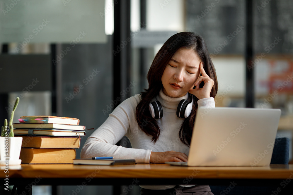 Asian women sitting in a home office With stress and eye strain.Tired businesswoman holding eyeglasses and massaging nose bridge. There are tablets, laptops, and coffee. Asian women sitting in a home office With stress and eye strain.Tired businesswoman holding eyeglasses and massaging nose bridge. There are tablets, laptops, and coffee.