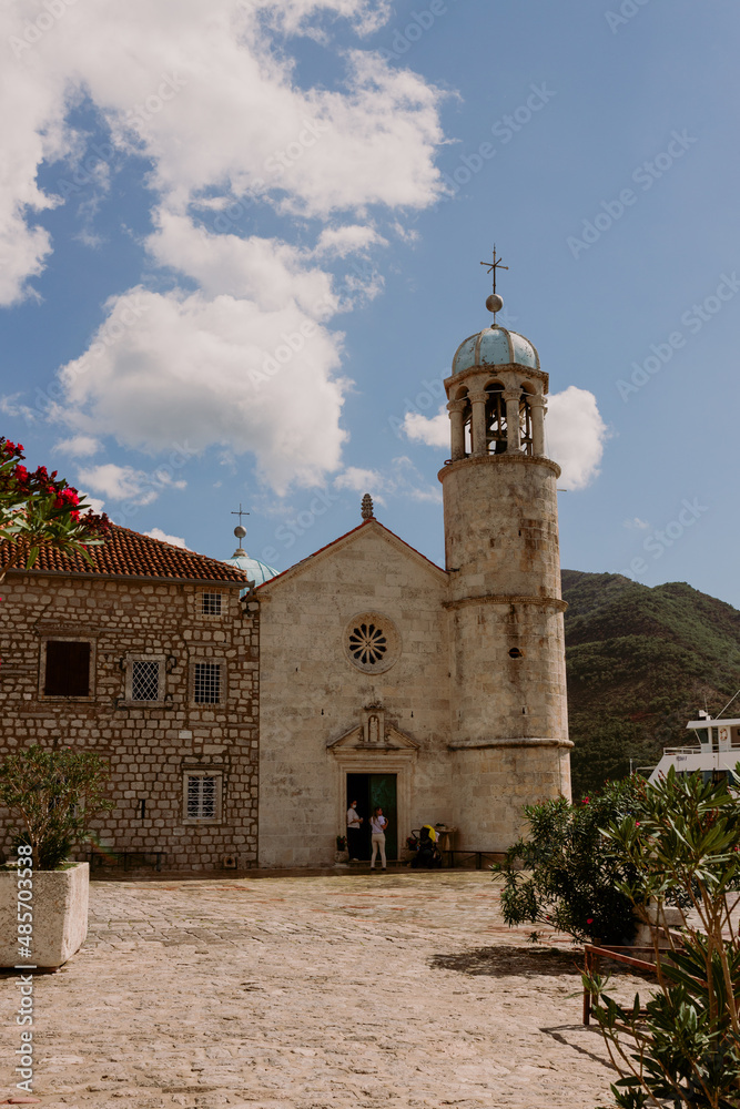 Perast, Montenegro - 15.09.2021: Roman catholic church our lady of the rocks on island islet in boka kotor bay in front of mountains range and blue sky, Montenegro. Unesco world heritage.