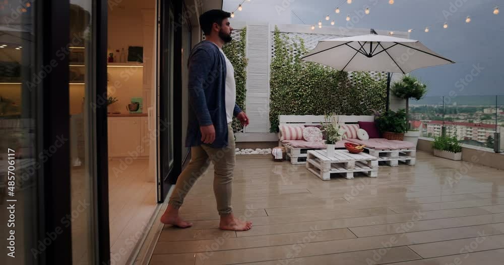 man opens sliding doors, going out on rooftop patio with cozy lounge ...