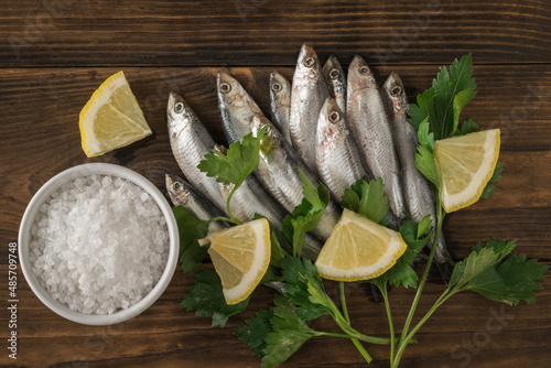 A bowl with coarse sea salt and sprat with herbs and lemon on a wooden table.