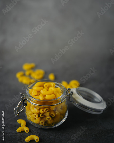 raw macaroni pasta in glass jar on black background