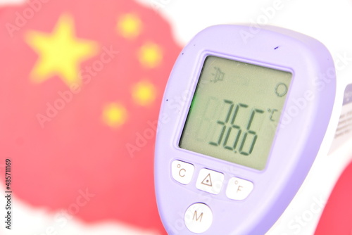 Concept of winter Games in 2022 in Beijing, China, due to threat of new coronavirus infection. Infrared thermometer shows healthy body temperature on background of red Chinese flag and map. Side view