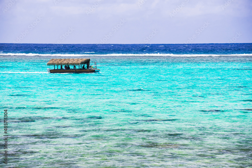 Tourist boat trip on a summer vacation to the tropical island of Rarotonga in the perfect crystal clear blue water of Muri Lagoon, Pacific Ocean, background with copy space
