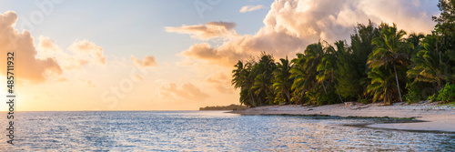 Tropical sandy beach at sunset with palm trees and dramatic clouds at sunset in the sky, Rarotonga, Cook Islands, background with copy space