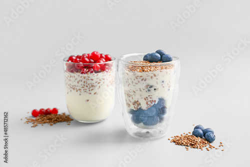 Glasses of sweet yogurt with flax seeds and berries on light background