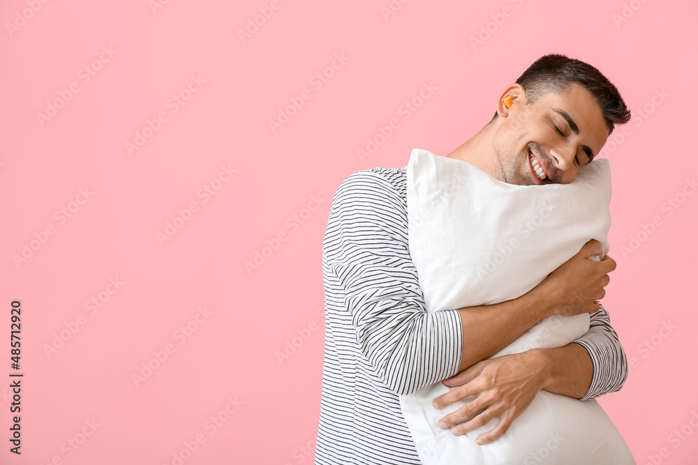 Young man with ear plugs and pillow on pink background Young man with ear plugs and pillow on pink background