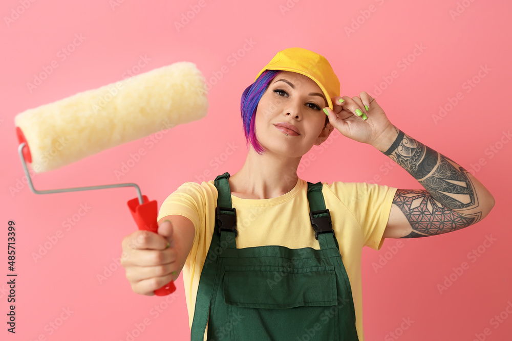 Female painter in cap with roller on pink background Female painter in cap with roller on pink background