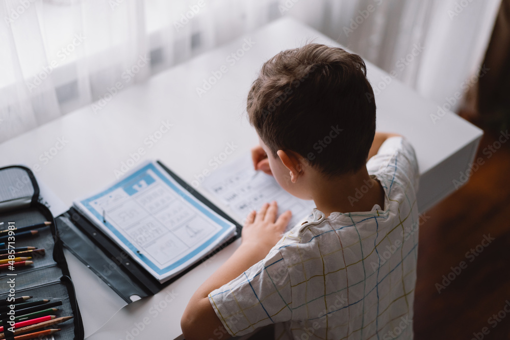 Distance learning education. Back to school. Cute kid boy studying at home and doing school homework. Thinking child sitting at table Distance learning education. Back to school. Cute kid boy studying at home and doing school homework. Thinking child sitting at table