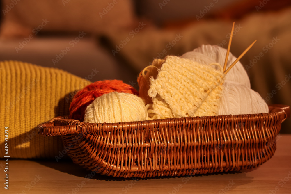 Wicker basket with knitting yarn and needles on table in room