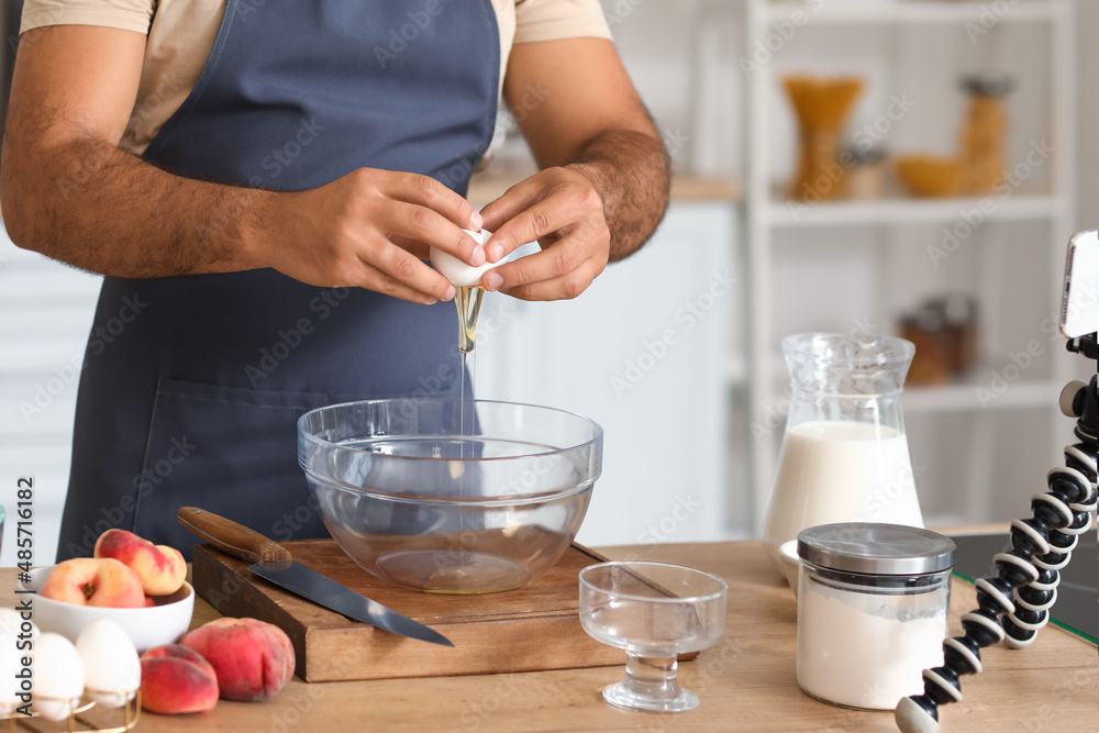 Young man breaking egg into bowl while following cooking video tutorial in kitchen, closeup Young man breaking egg into bowl while following cooking video tutorial in kitchen, closeup